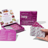 The image shows a dietary supplement product for Key Menstrual Cycle, with packaging that includes a box and a blister pack with tablets. A hand is holding the blister pack.